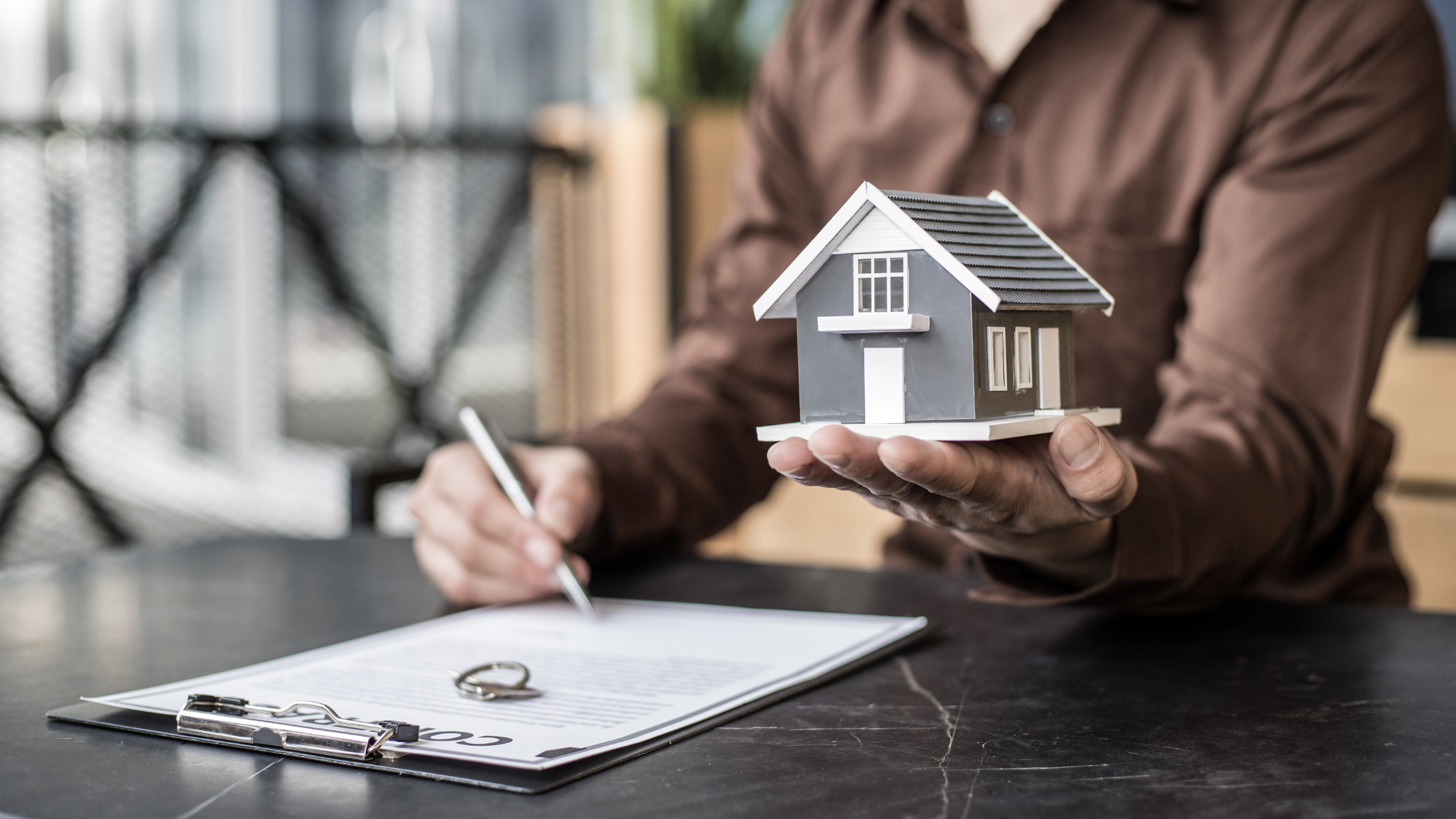 Person signing contract while holding house model